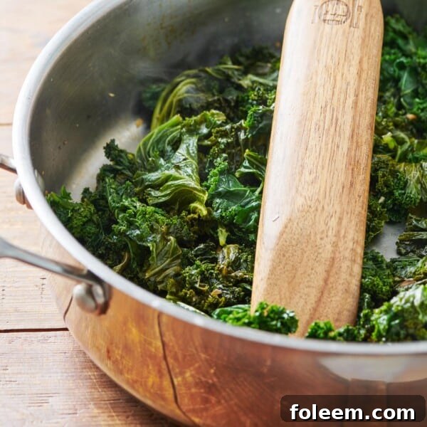 Cooked Kale in a pan with a wooden spatula.