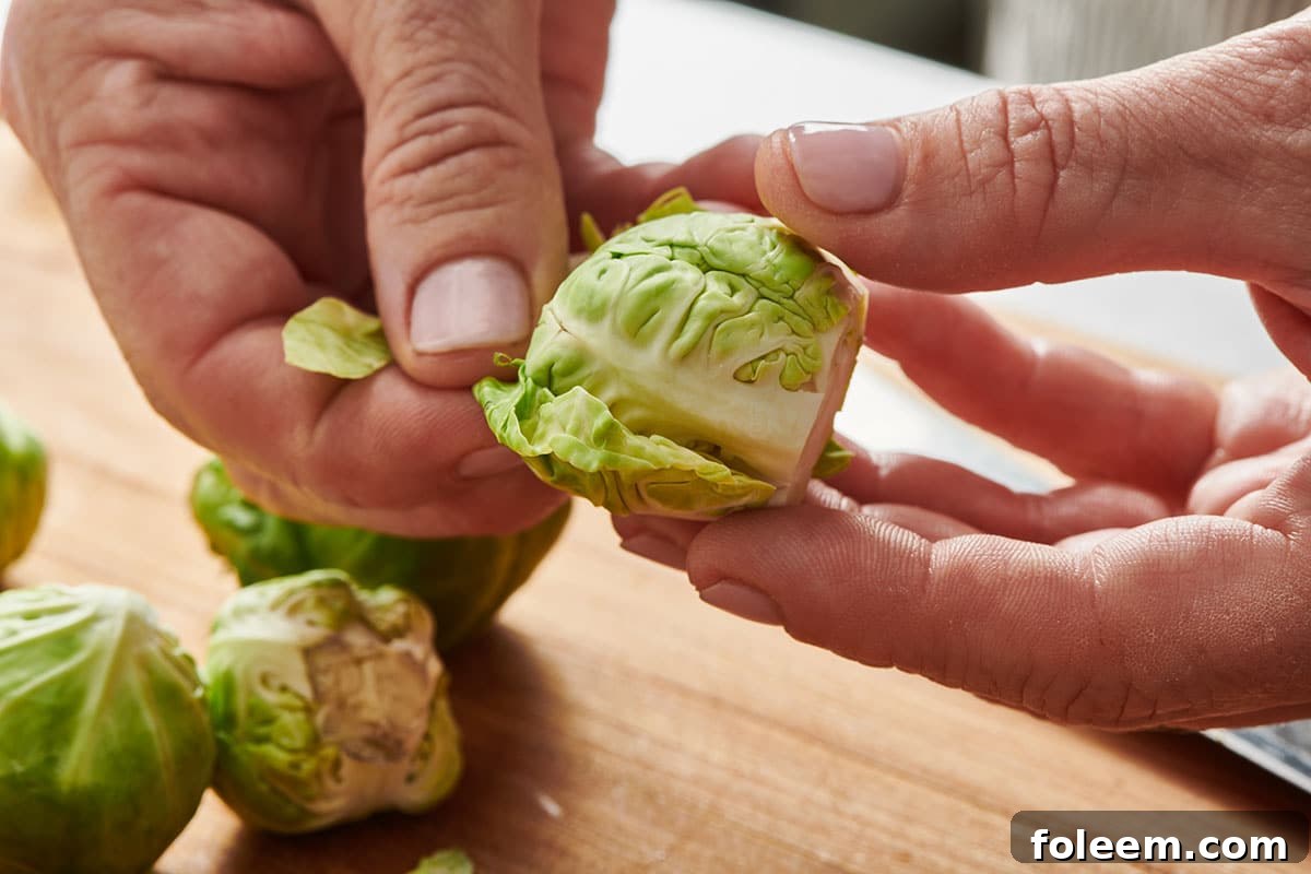 Woman removing out leaves from fresh Brussels sprouts.
