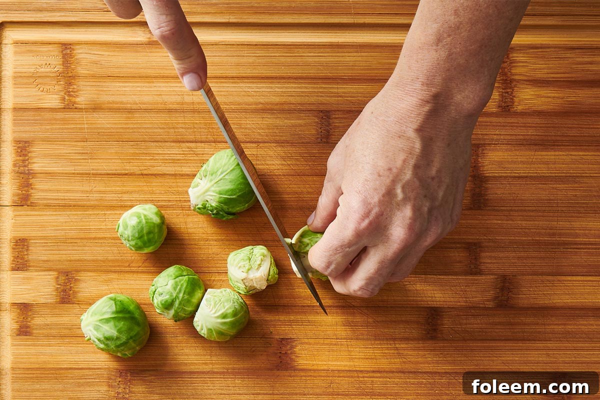 Woman cutting ends off fresh Brussels sprouts with knife.