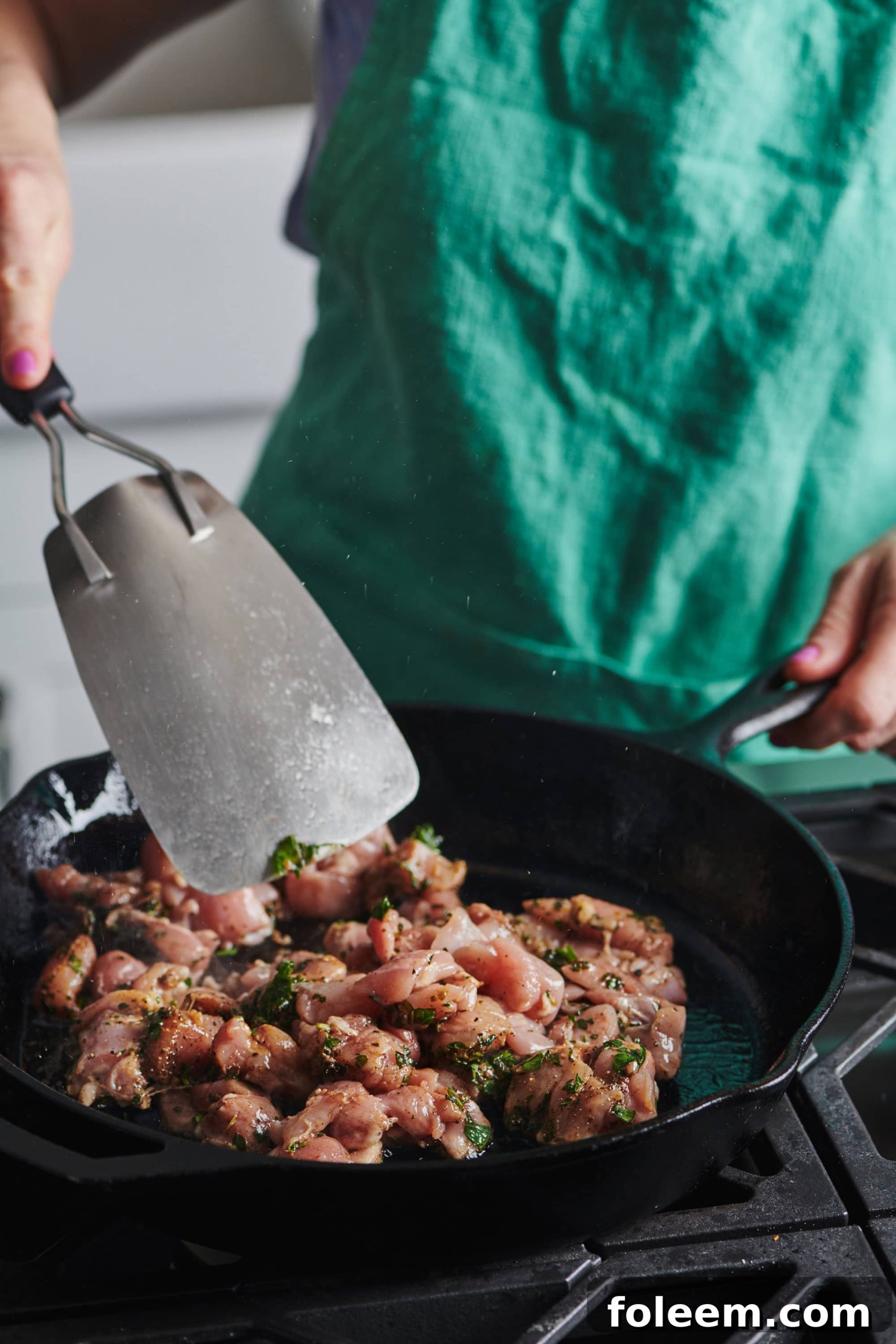 Metal spatula flipping Chicken Kawarma in a skillet.