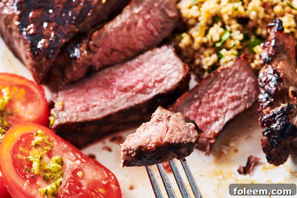 Fork with piece of sliced grilled NY strip steak over plate.