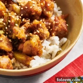 Homemade General Tso's Chicken over rice with sesame seed garnish in brown bowl.