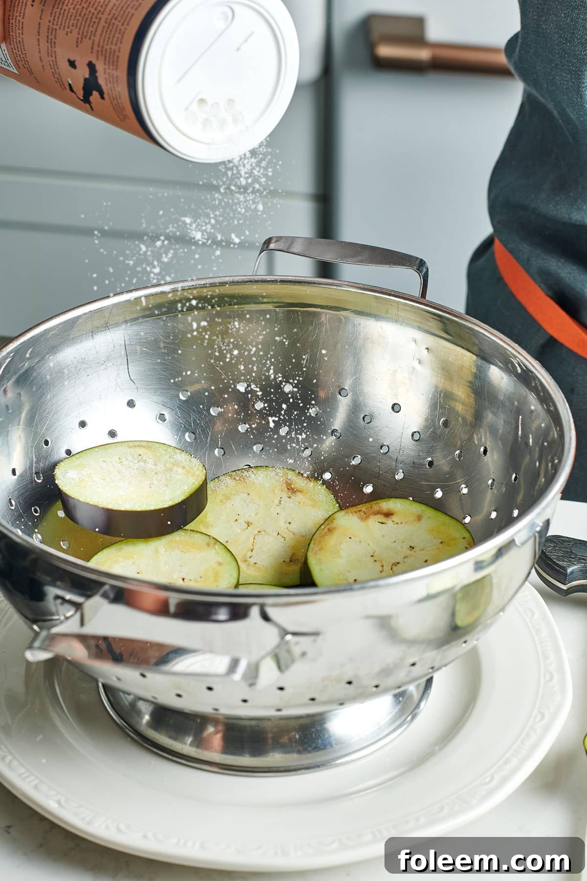 Pouring salt onto eggplant slices in metal colander.