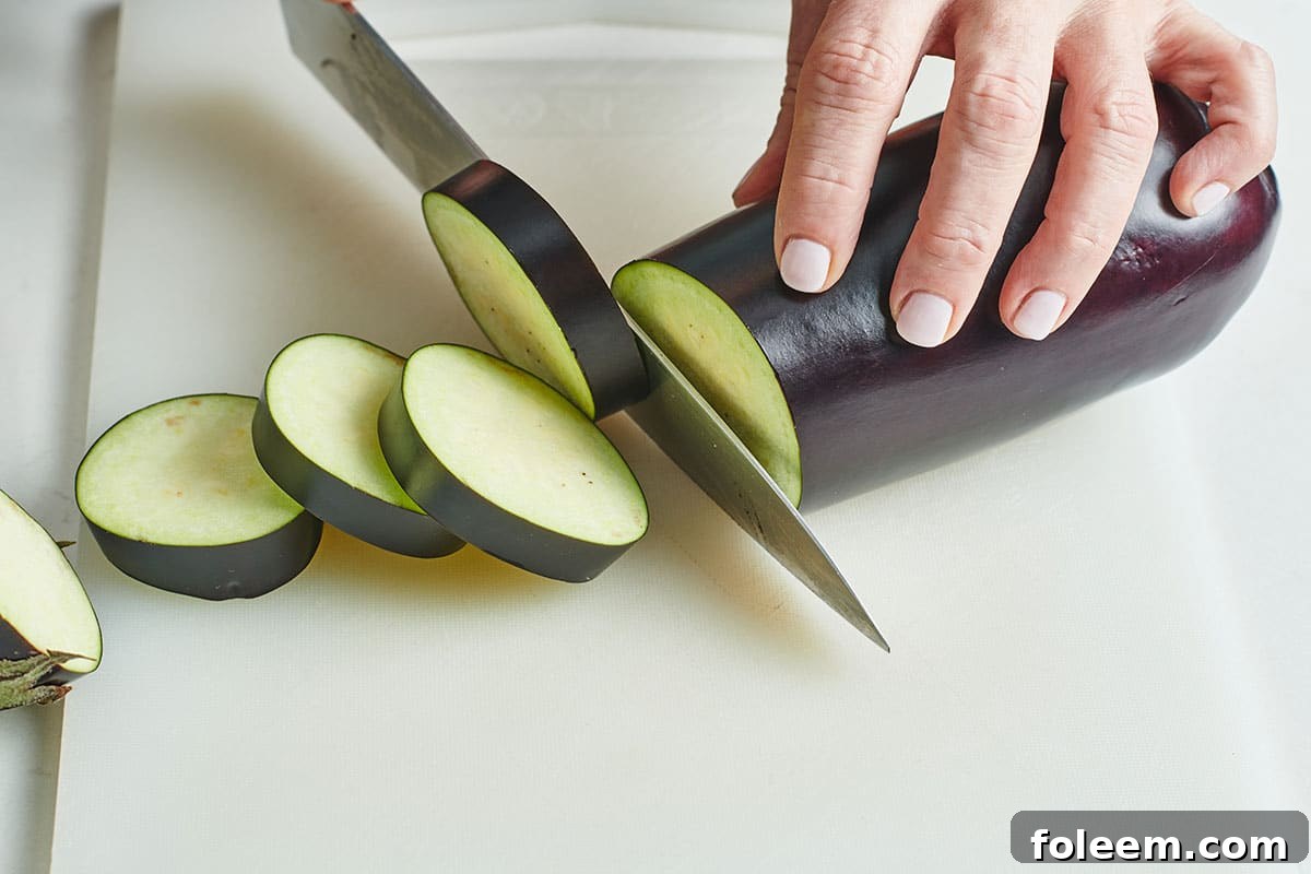 Katie Workman slicing fresh eggplant on cutting board with knife. 