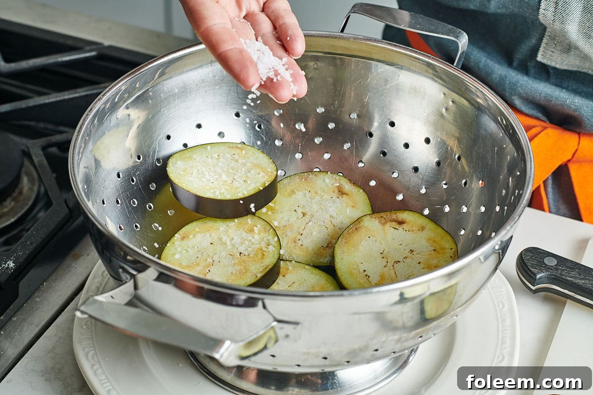 Adding salt to eggplant slices in colander.