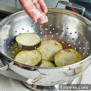 Adding salt to eggplant slices in colander.