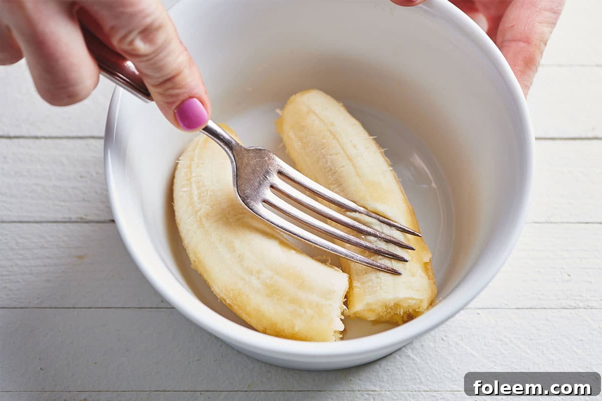 Woman mashing bananas in white bowl with fork.