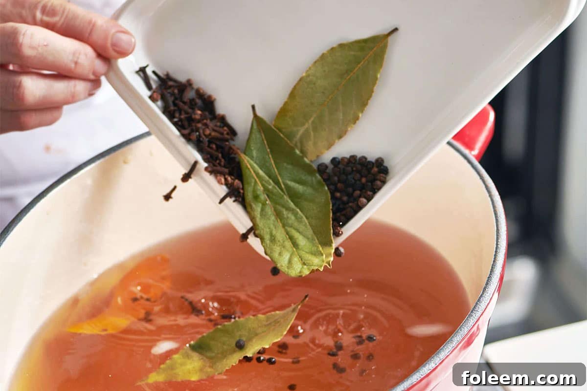 Pouring bay leaves and other herbs and spices into pot of homemade broth.