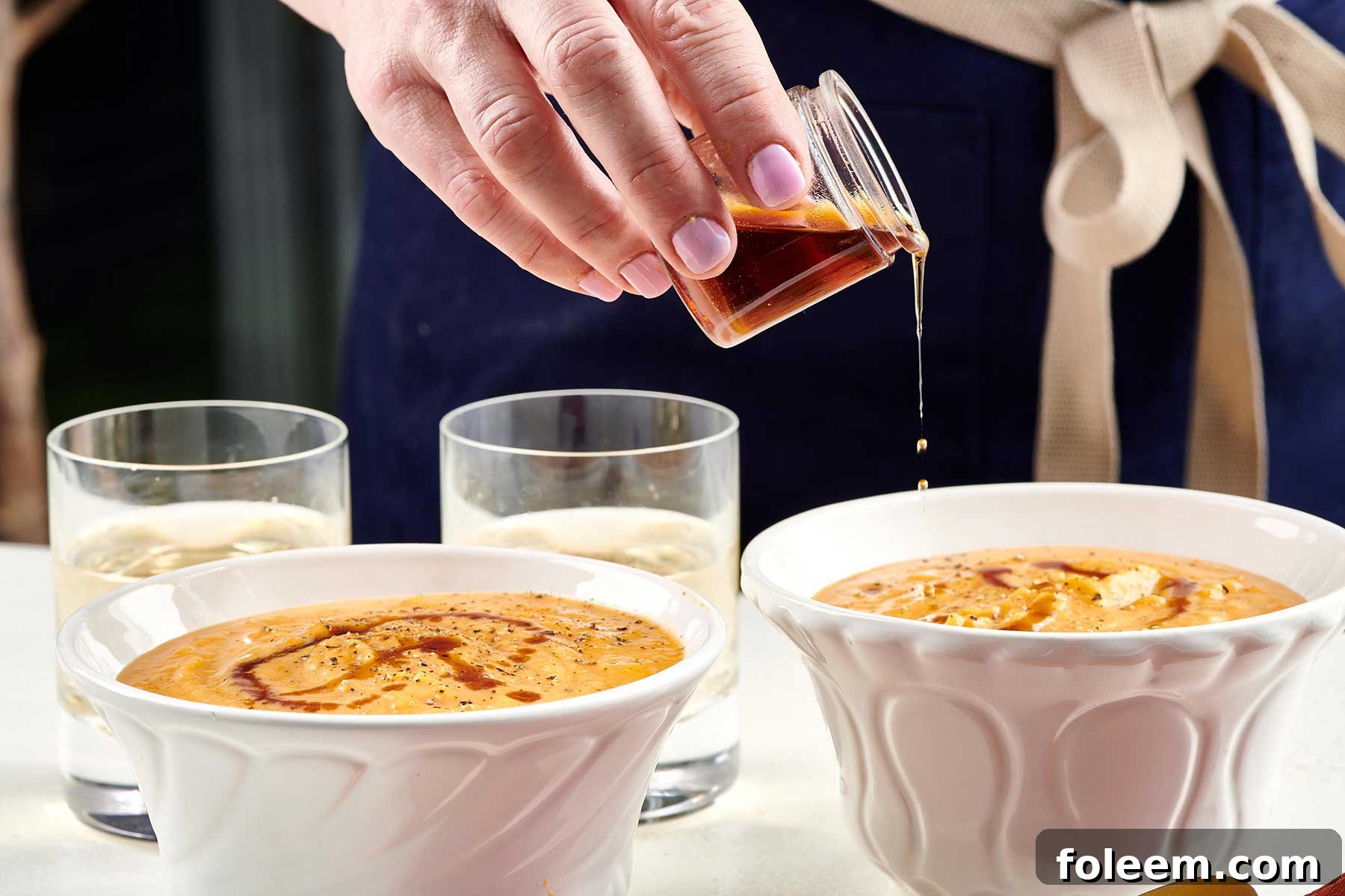 Pouring maple syrup over butternut squash soup in white bowls.