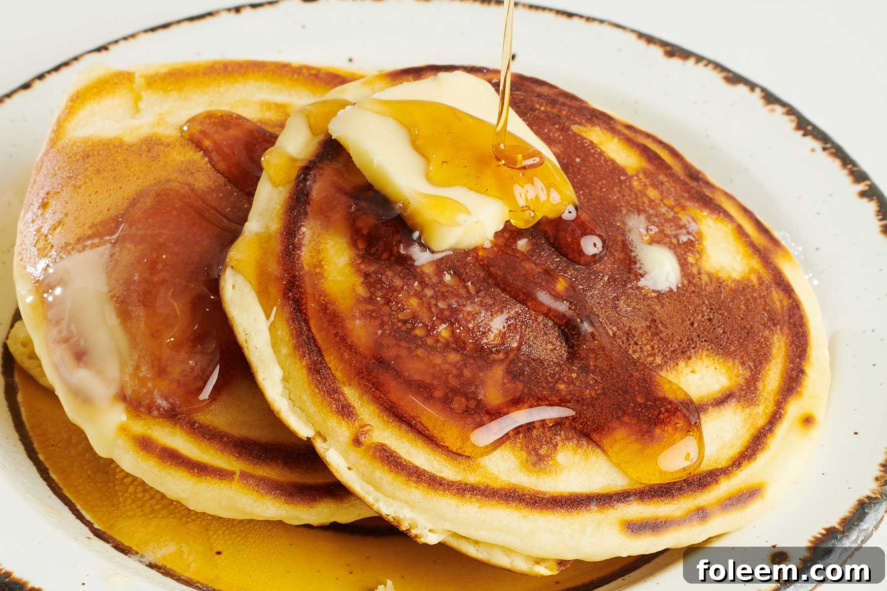 Syrup pouring over homemade pancakes and butter.