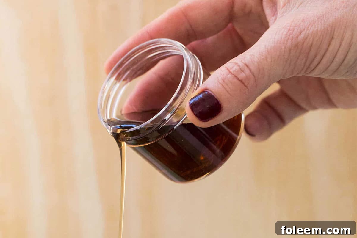 Woman pouring maple syrup from small glass jar.