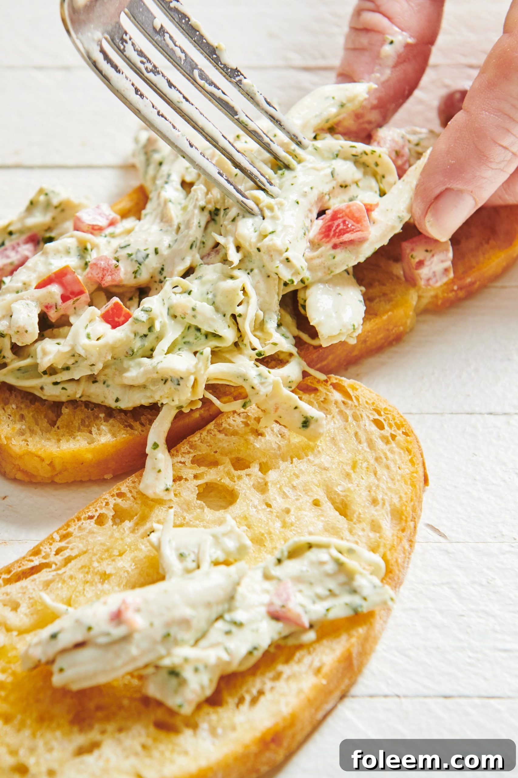 Spreading Herbed Chicken Salad onto toasted bruschetta with fork.