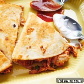 BBQ chicken quesadillas on plate with spoons of barbecue sauce and sour cream.