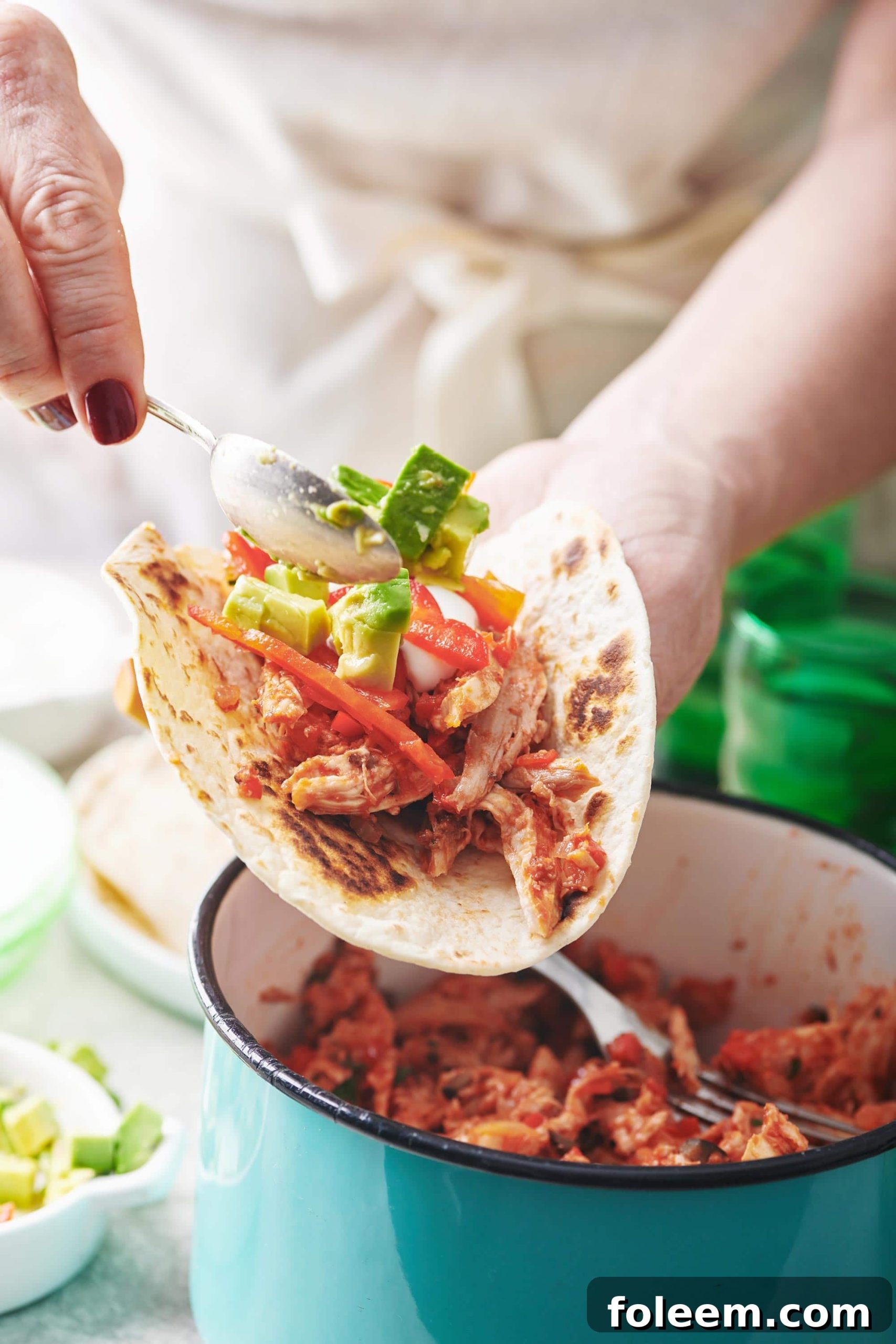 Spoon scooping avocado onto a Shredded Chicken Taco.