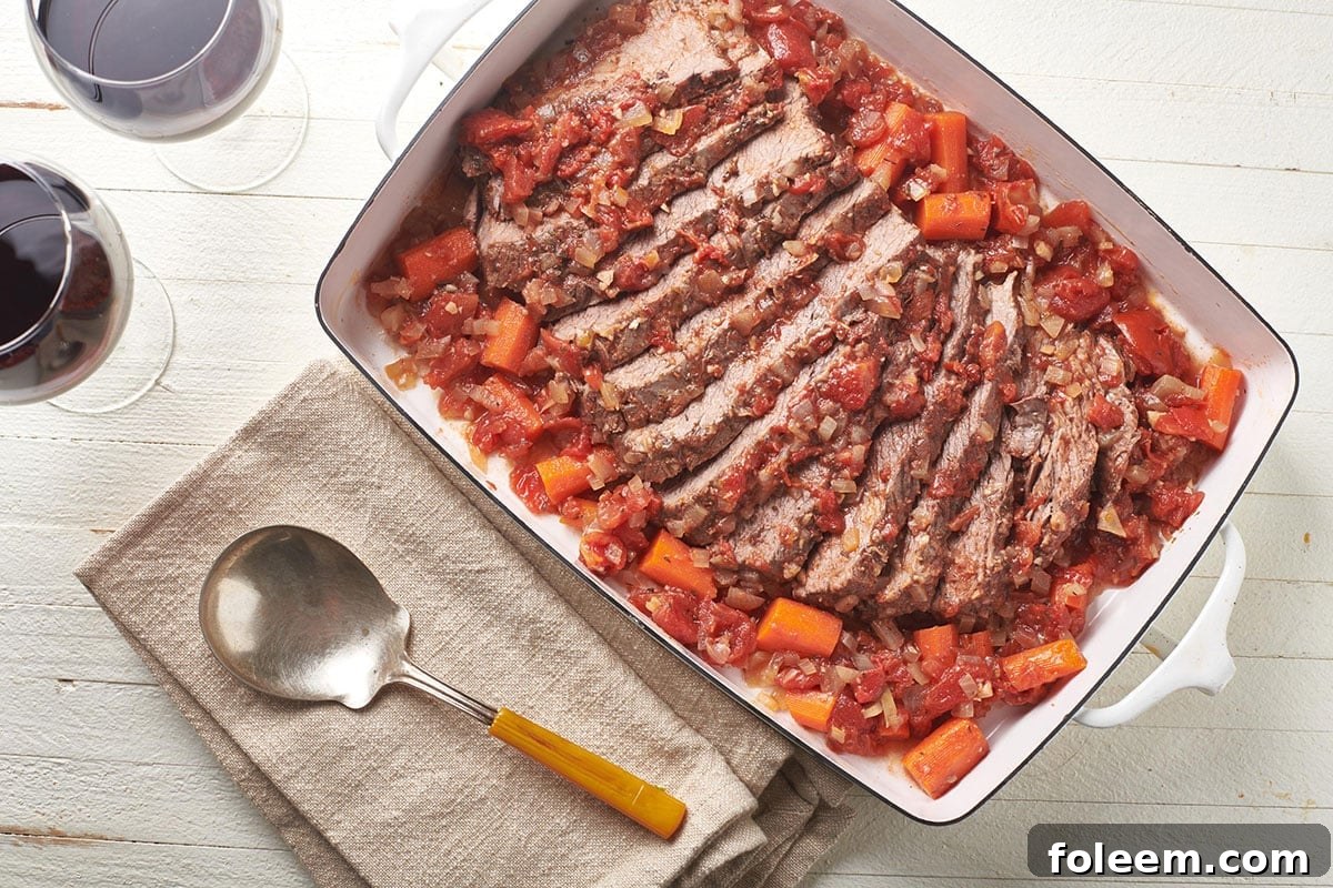 Jewish-style brisket in white dish on table with serving spoon.