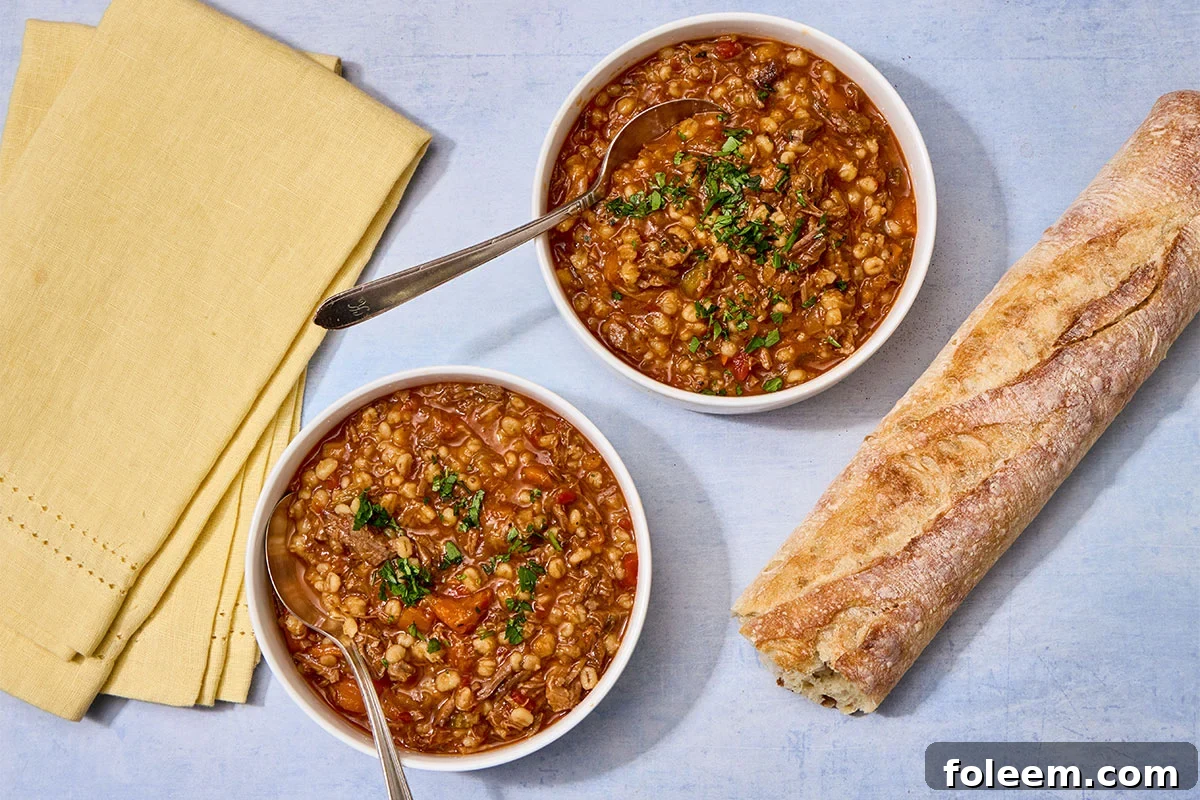 Brisket barley soup in bowls on table with bread.
