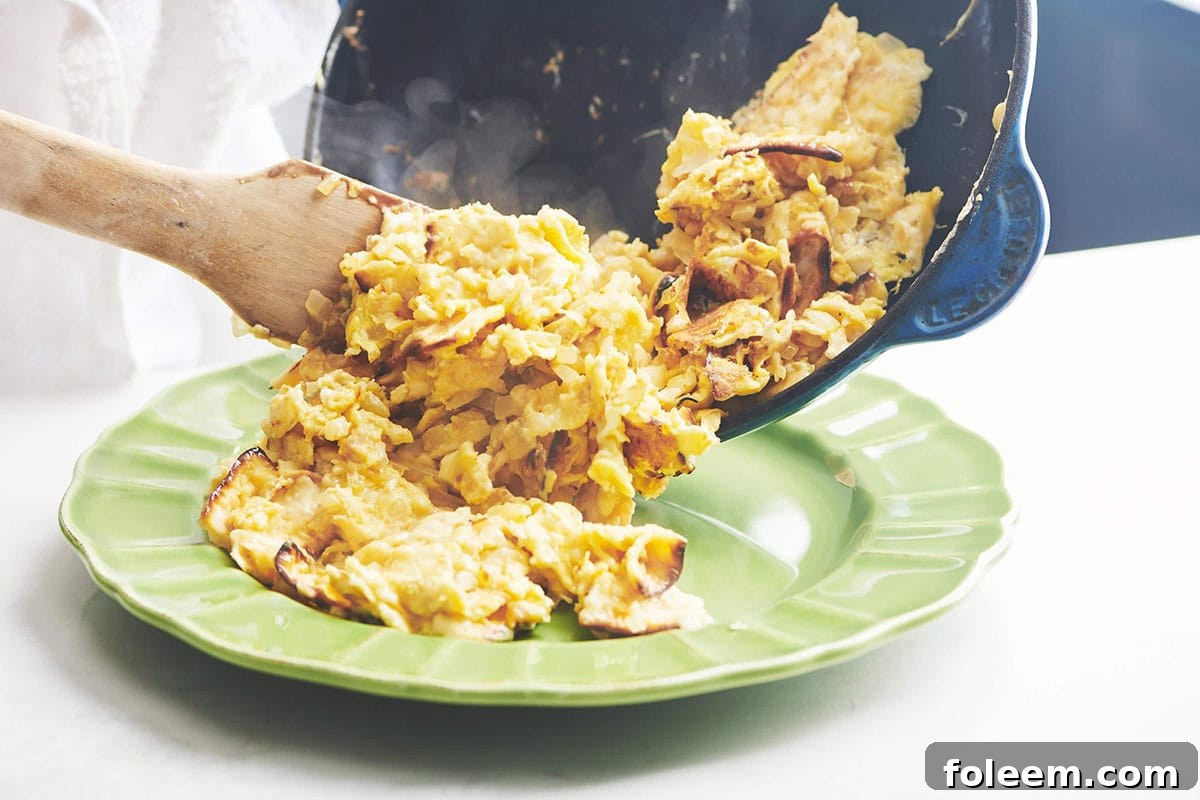 Wooden spatula pushing Matzoh Brei from a skillet to a plate.