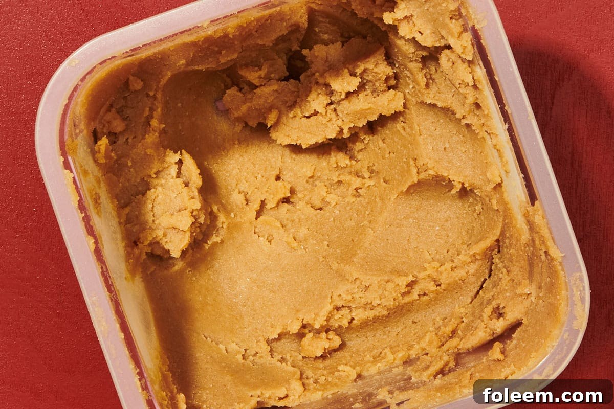 Plastic tub of red miso paste on bright red table.