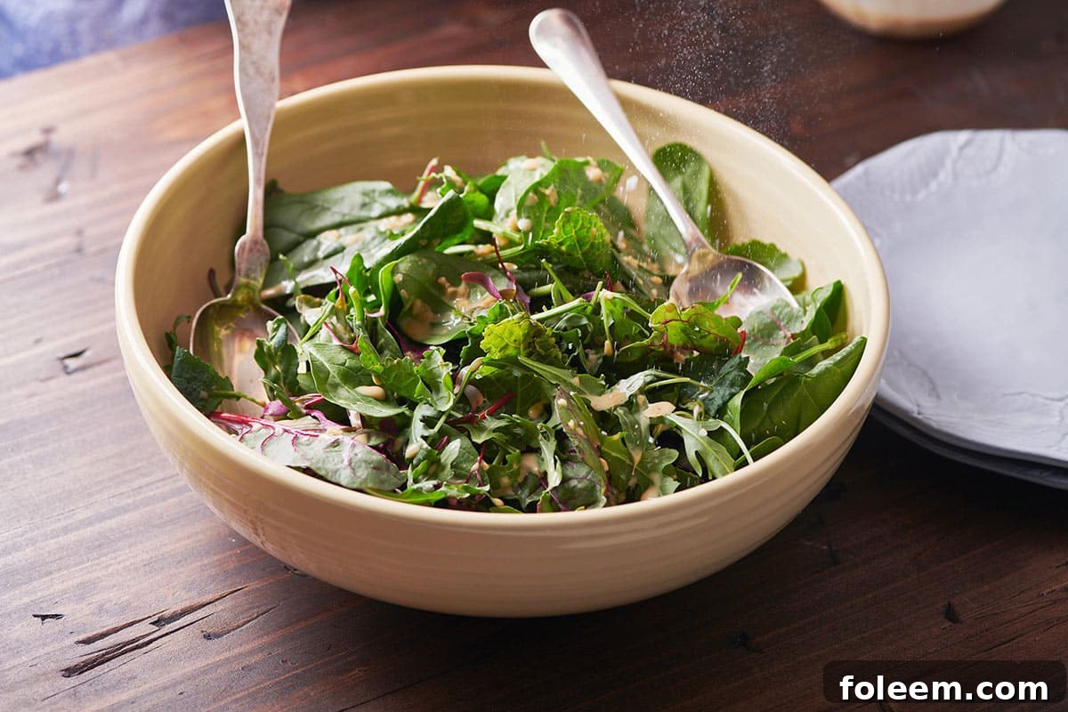 Mixed Green Salad with Creamy Sesame Dressing in brown serving bowl on table with spoons.