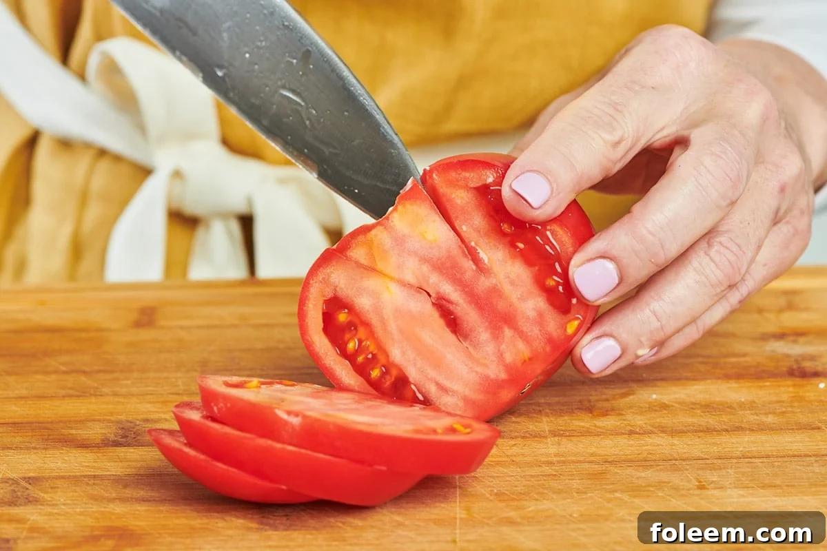 Katie Workman cutting stem out of large ripe tomato with knife on cutting board.
