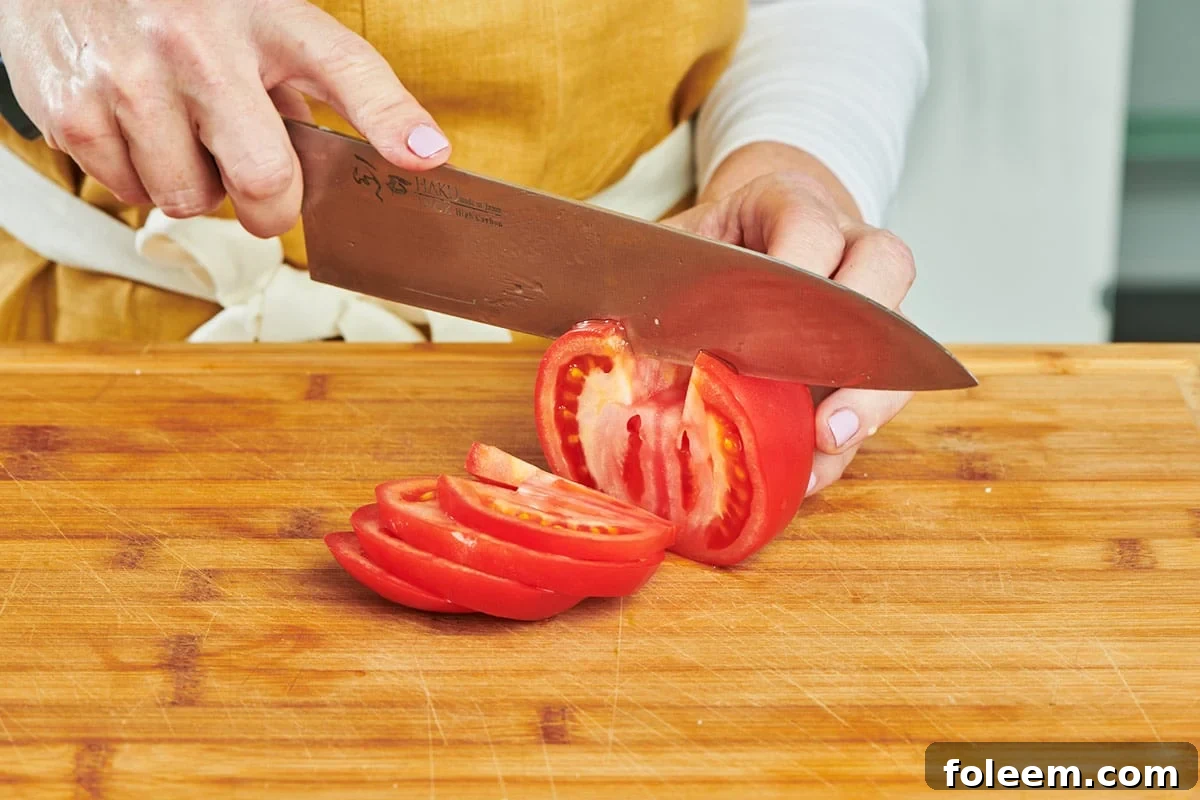 Katie Workman slicing large red tomato on cutting board with chef's knife.
