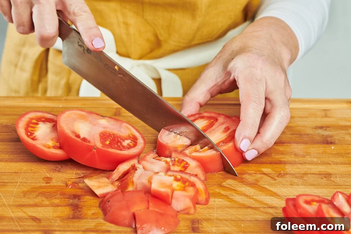 Katie Workman dicing sliced tomatoes on cutting board with chef's knife.