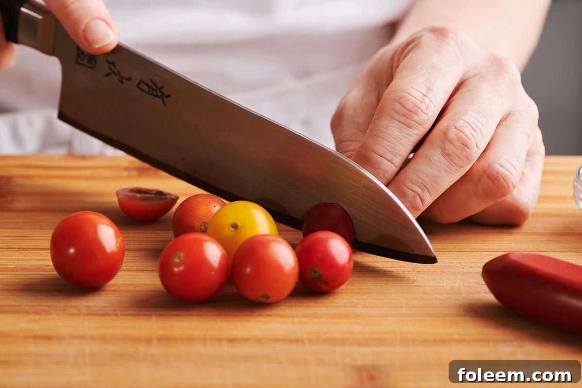 Slicing cherry tomatoes with large chefs knife on wood cutting board.