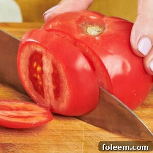 Katie Workman slicing large tomato with chef's knife on cutting board.