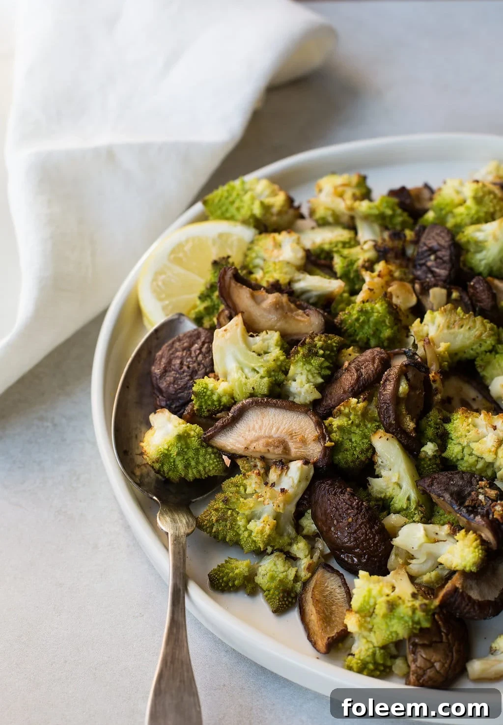 Roasted Broccoflower and Shiitake Mushrooms with Rosemary and Garlic in white bowl with spoon.