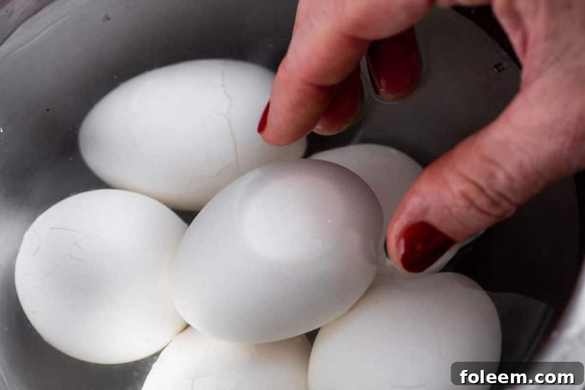 Woman placing boiled eggs in ice water bath.