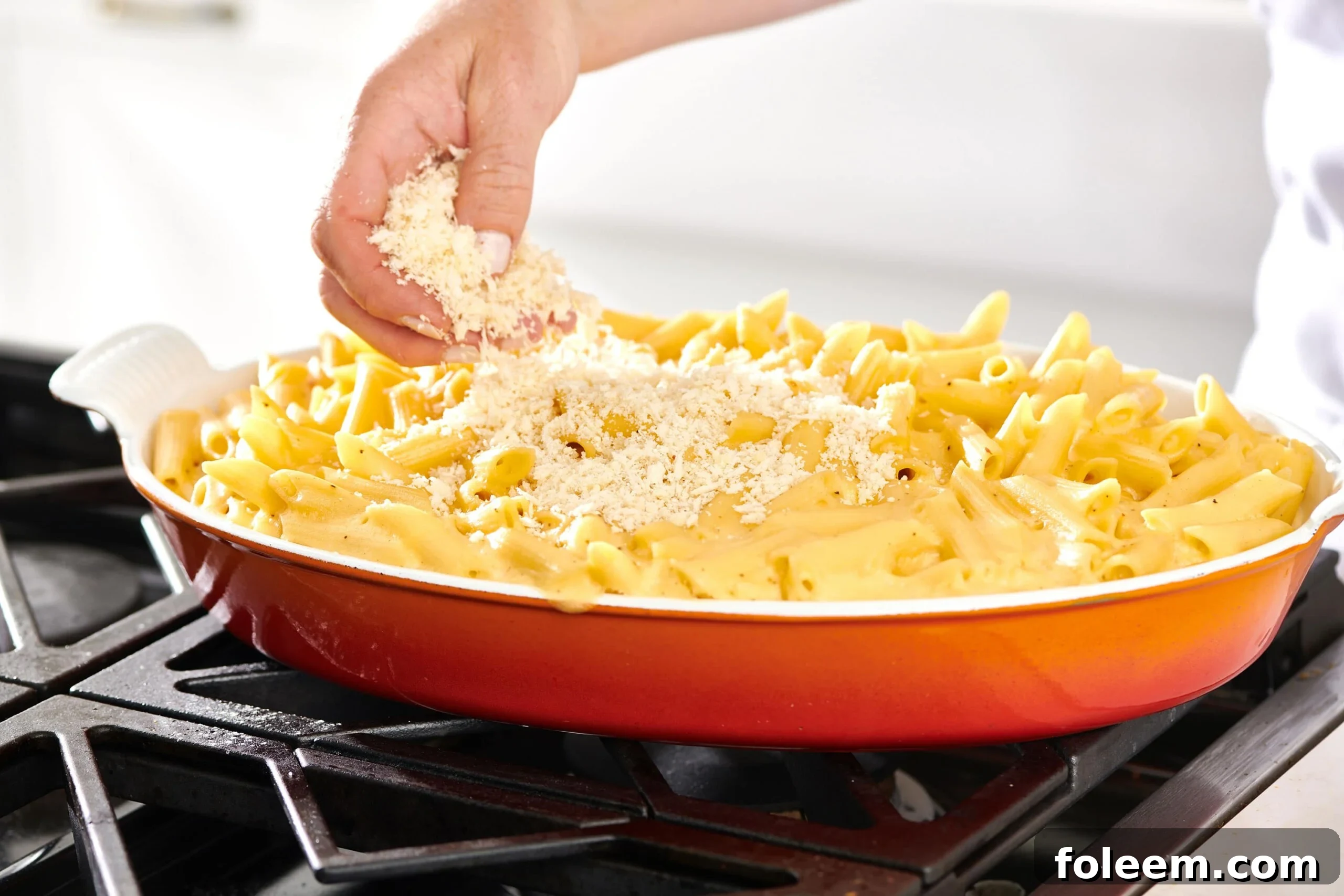 Woman sprinkling panko topping onto a baking pan of macaroni and cheese.