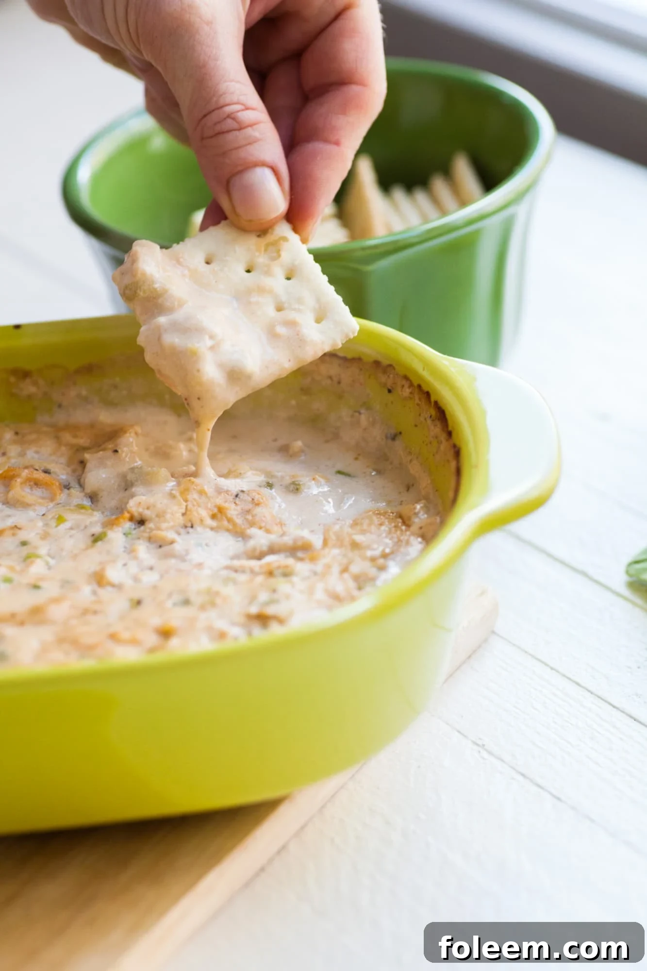 Dipping cracker in bowl of Hot Clam Dip.