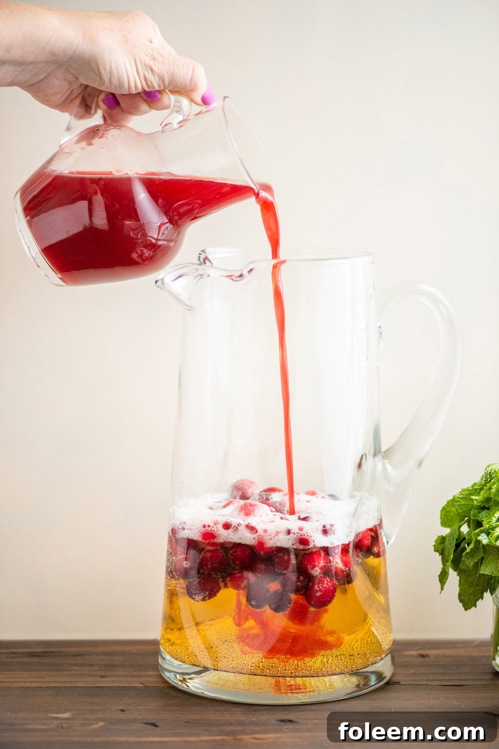 Pouring cranberry juice into pitcher for a Cranberry Orange Shrub.