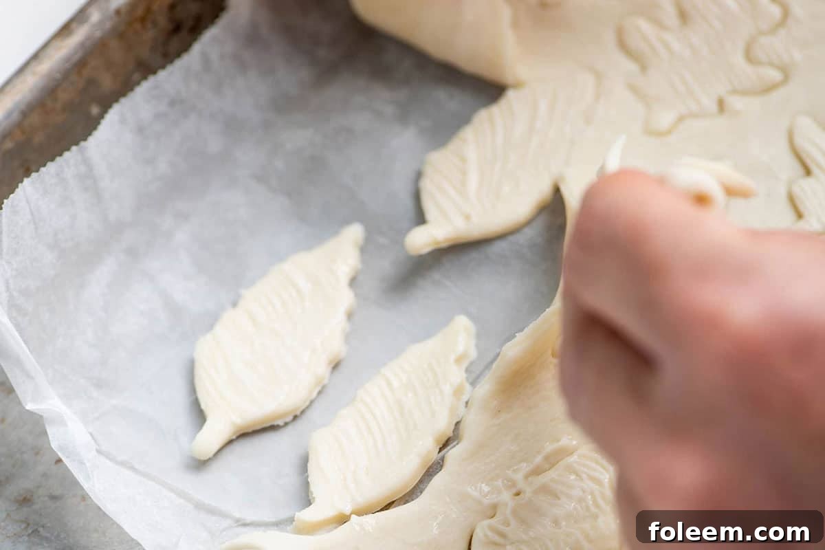 Woman removing excess puff pastry from leaf cutouts.