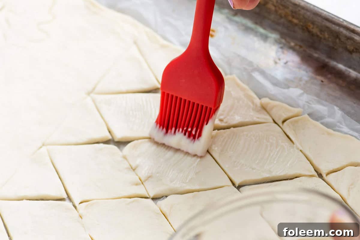 Red brush brushing mayonnaise onto cut puff pastry dough.