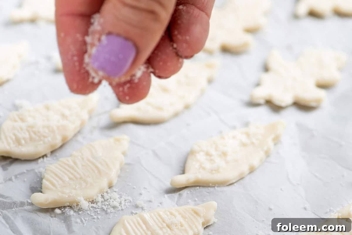 Woman sprinkling parmesan cheese onto puff pastry dough cut-outs.