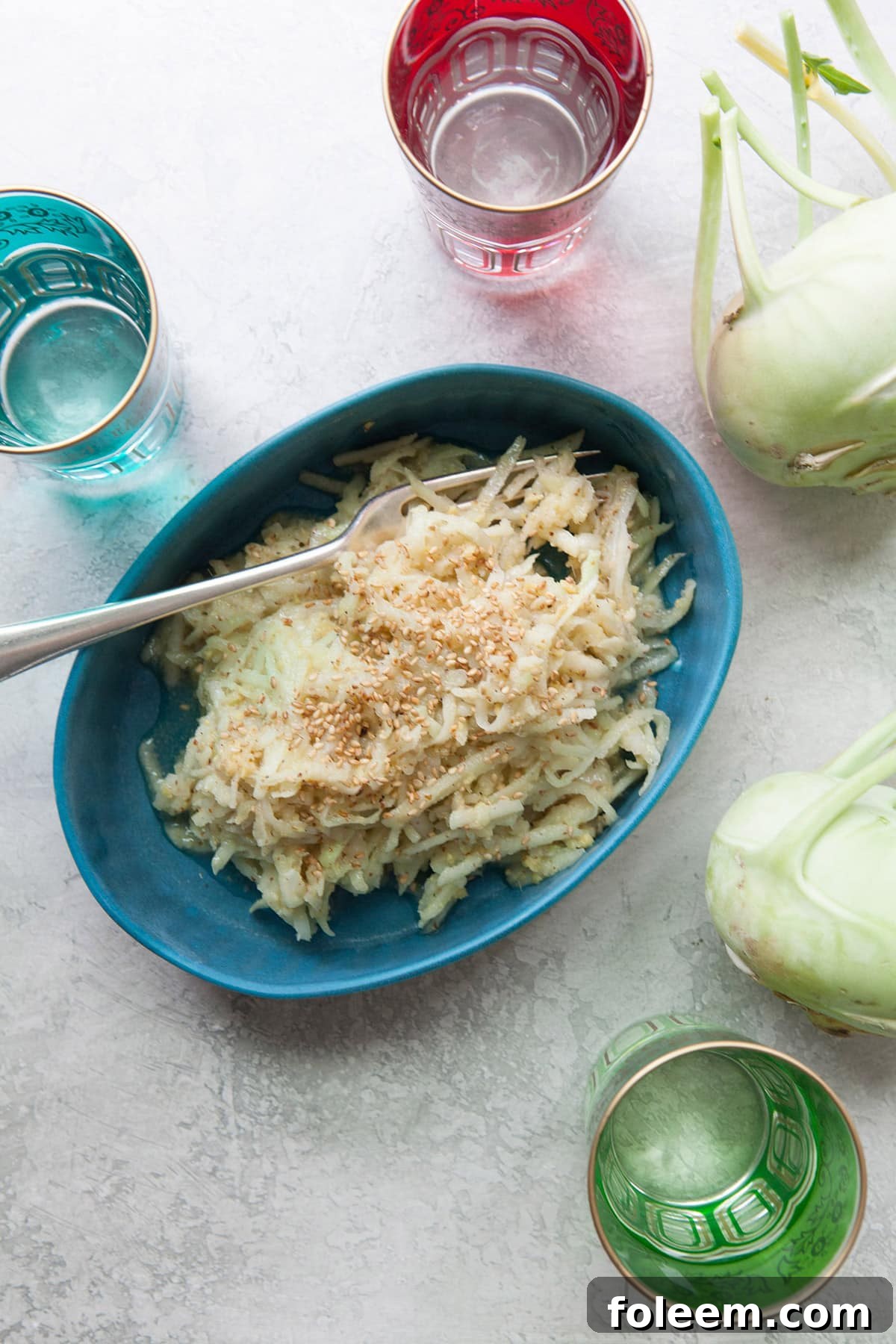 Asian Kohlrabi and Apple Slaw in a blue bowl with a serving fork with whole kohlrabi nearby.