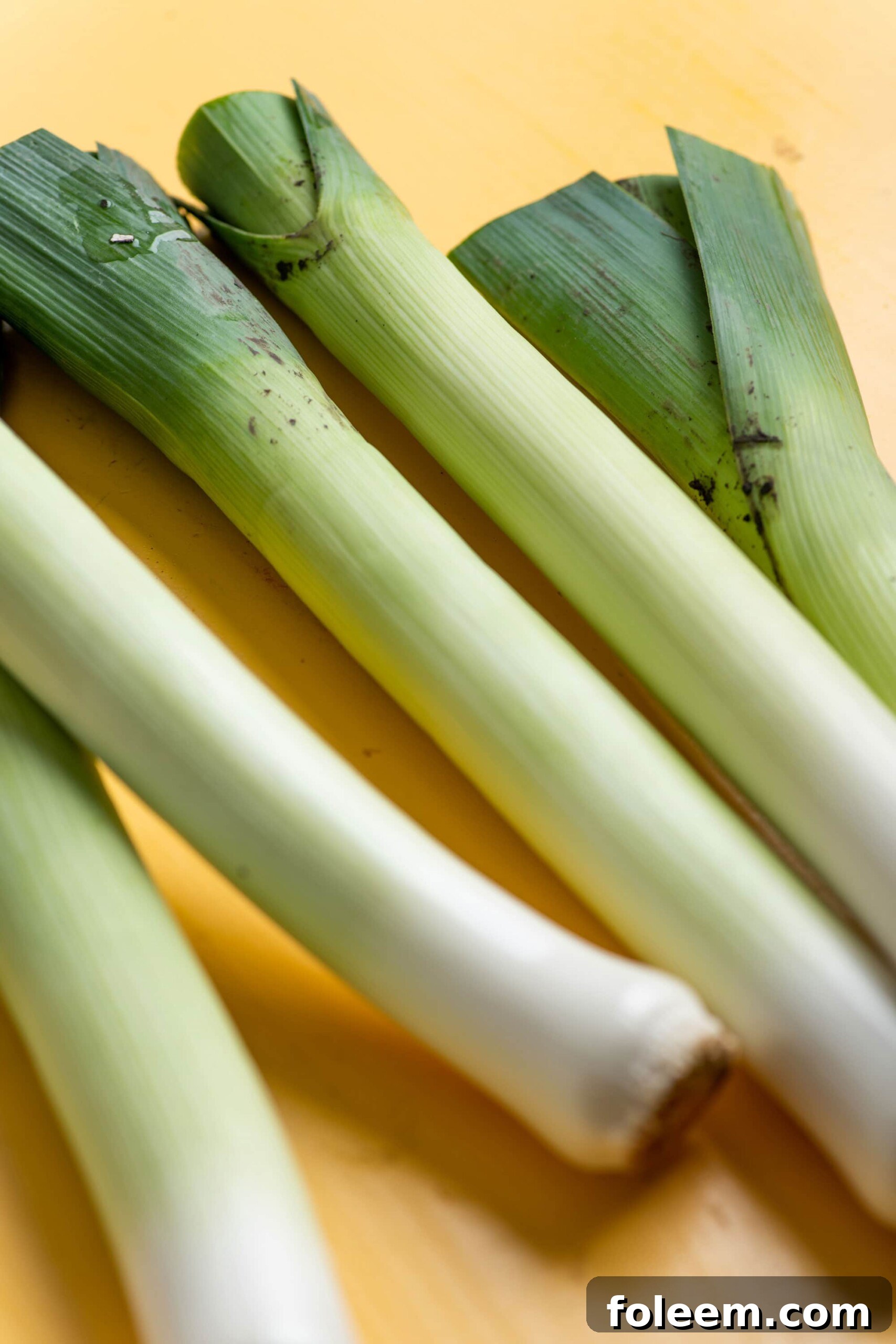 Unwashed leeks on a yellow surface.