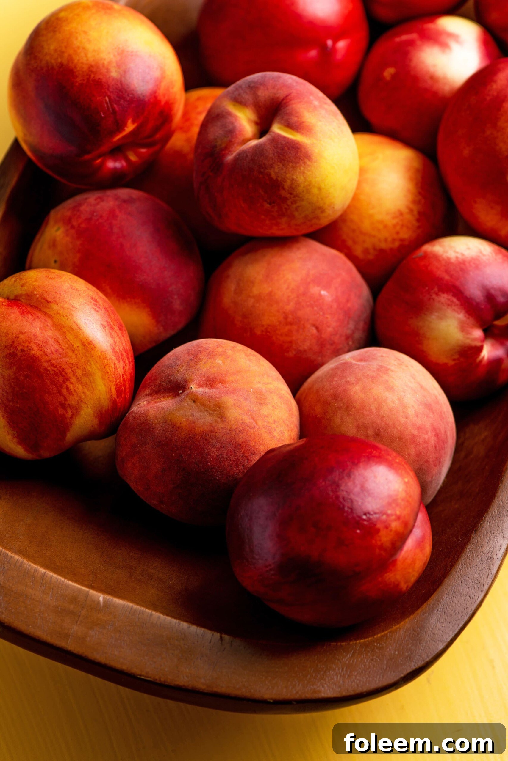 Peaches and Nectarines piled on a wooden bowl.