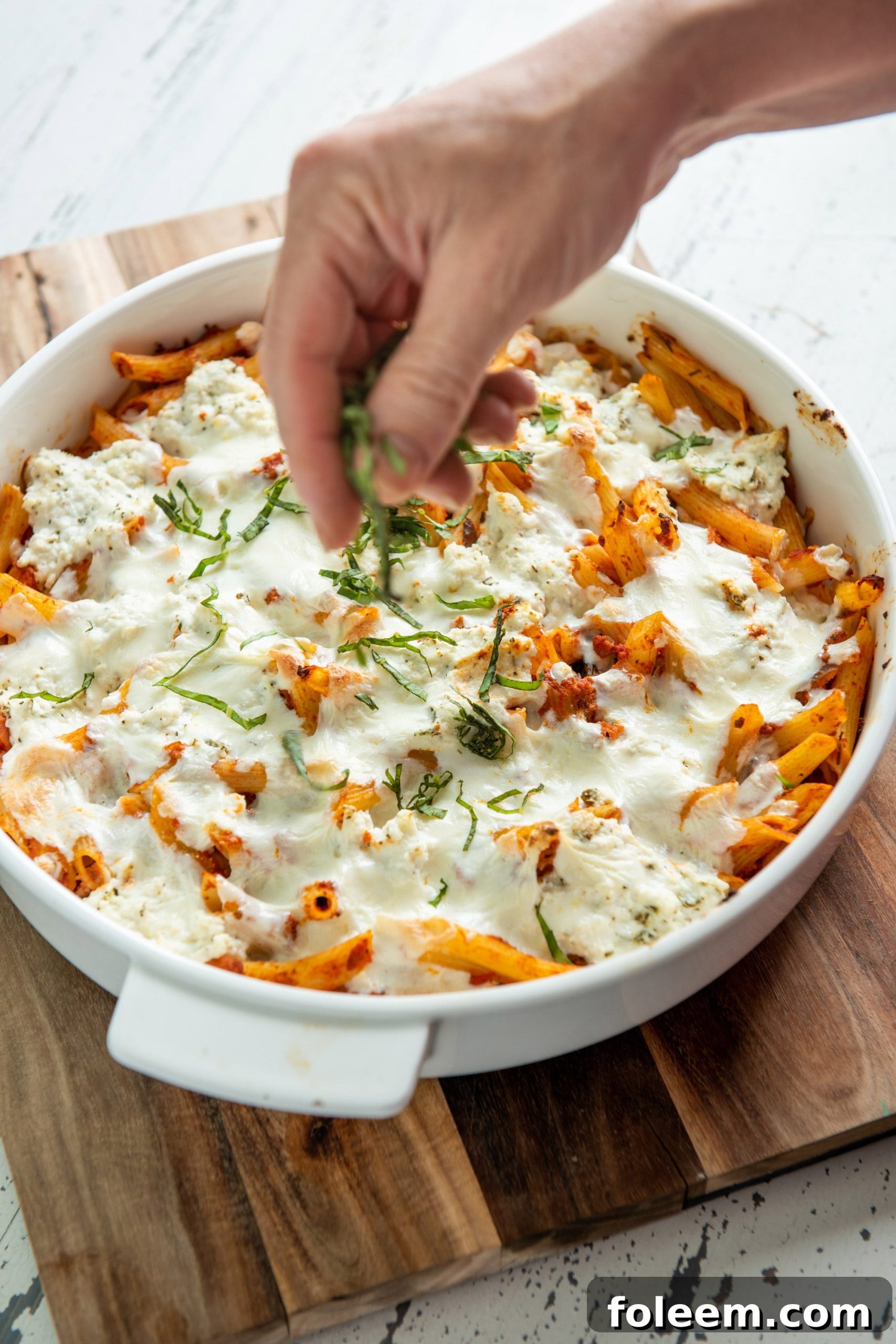 Sprinkling chiffonaded basil over Baked Pasta with Bolognese Sauce in casserole dish.