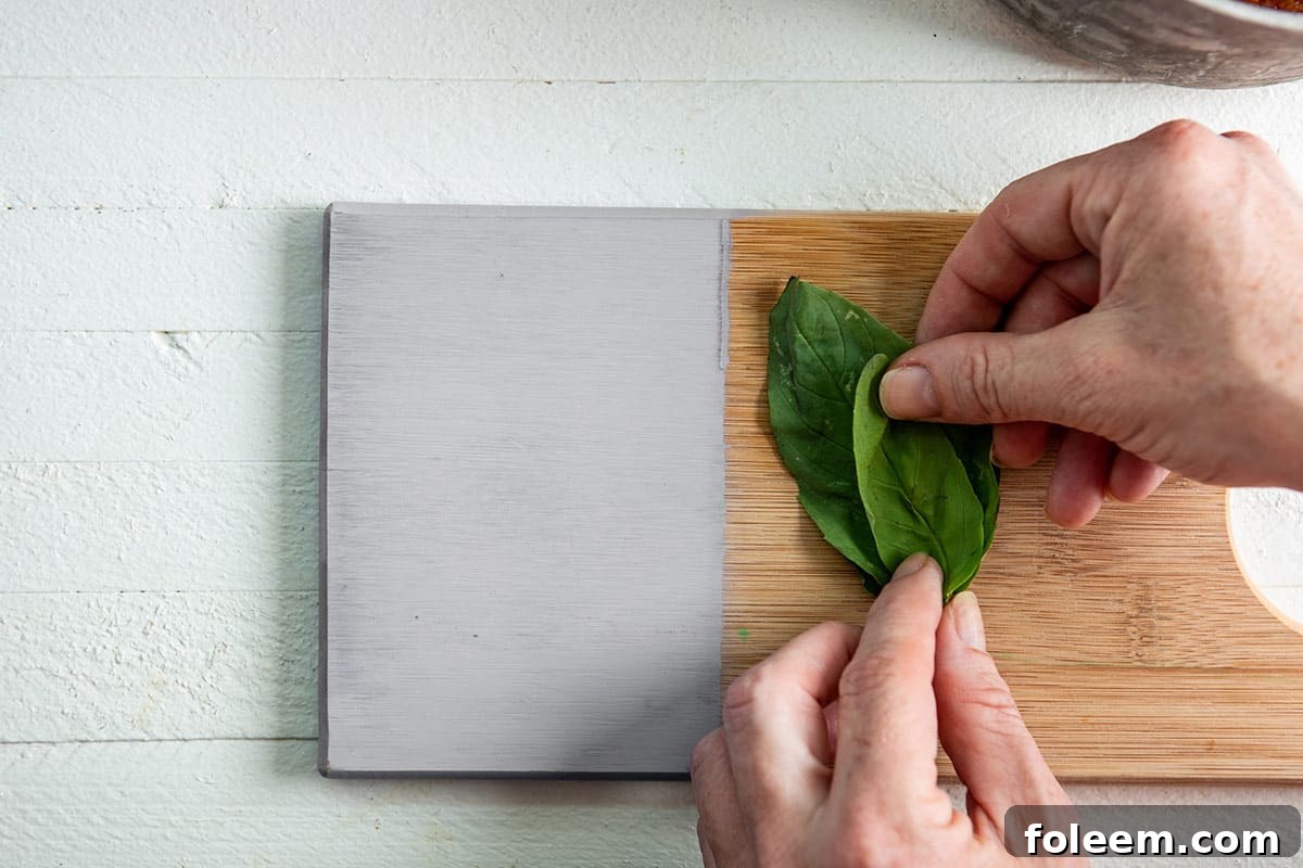 Stacking fresh basil leaves on wood cutting board.