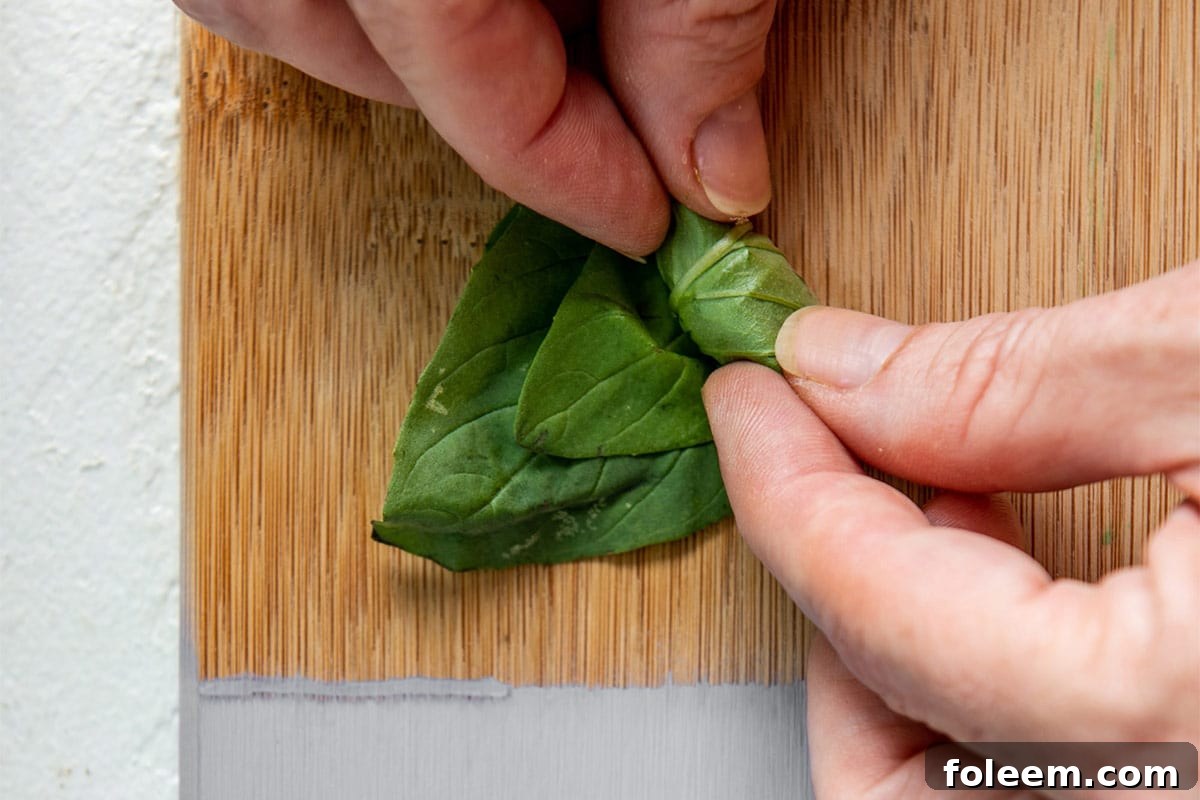 Rolling a stack of fresh basil leaves on cutting board.