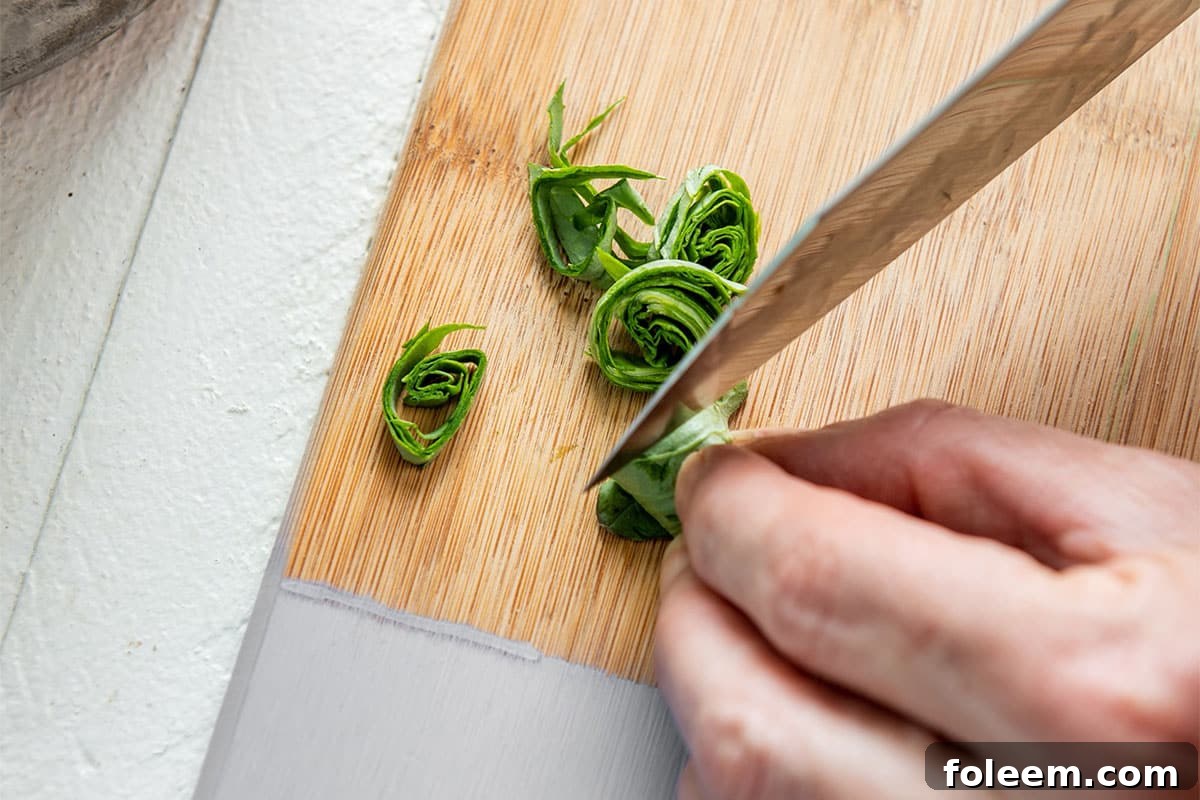 Cutting rolled basil leaves with sharp knife to chiffonade.