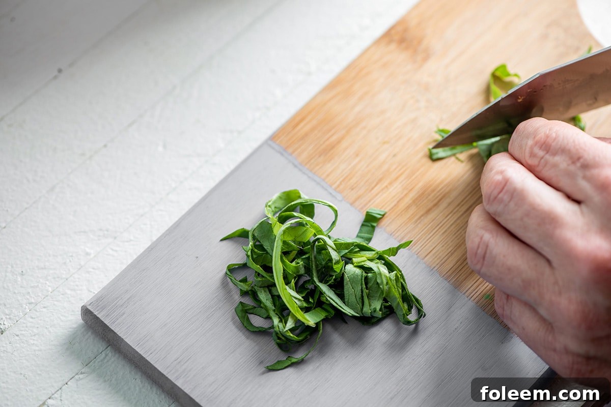 Final cuts of chiffonade basil on wood cutting board.
