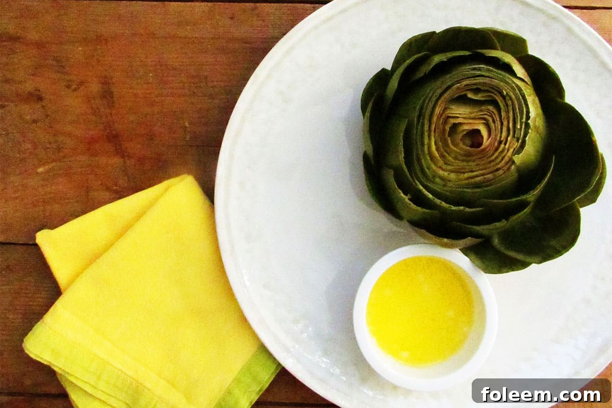 Steamed artichoke on plate with melted butter in bowl.