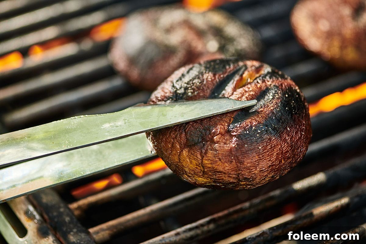 Flipping portobello mushrooms on grill grates with tongs.