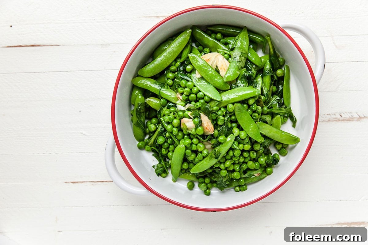 Green peas, sugar snap peas, garlic, arugula, and spinach in white bowl.