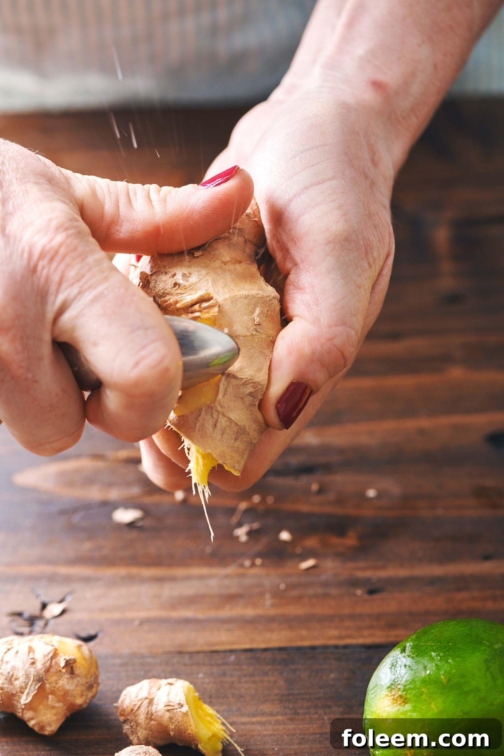 Woman peeling ginger root with spoon.