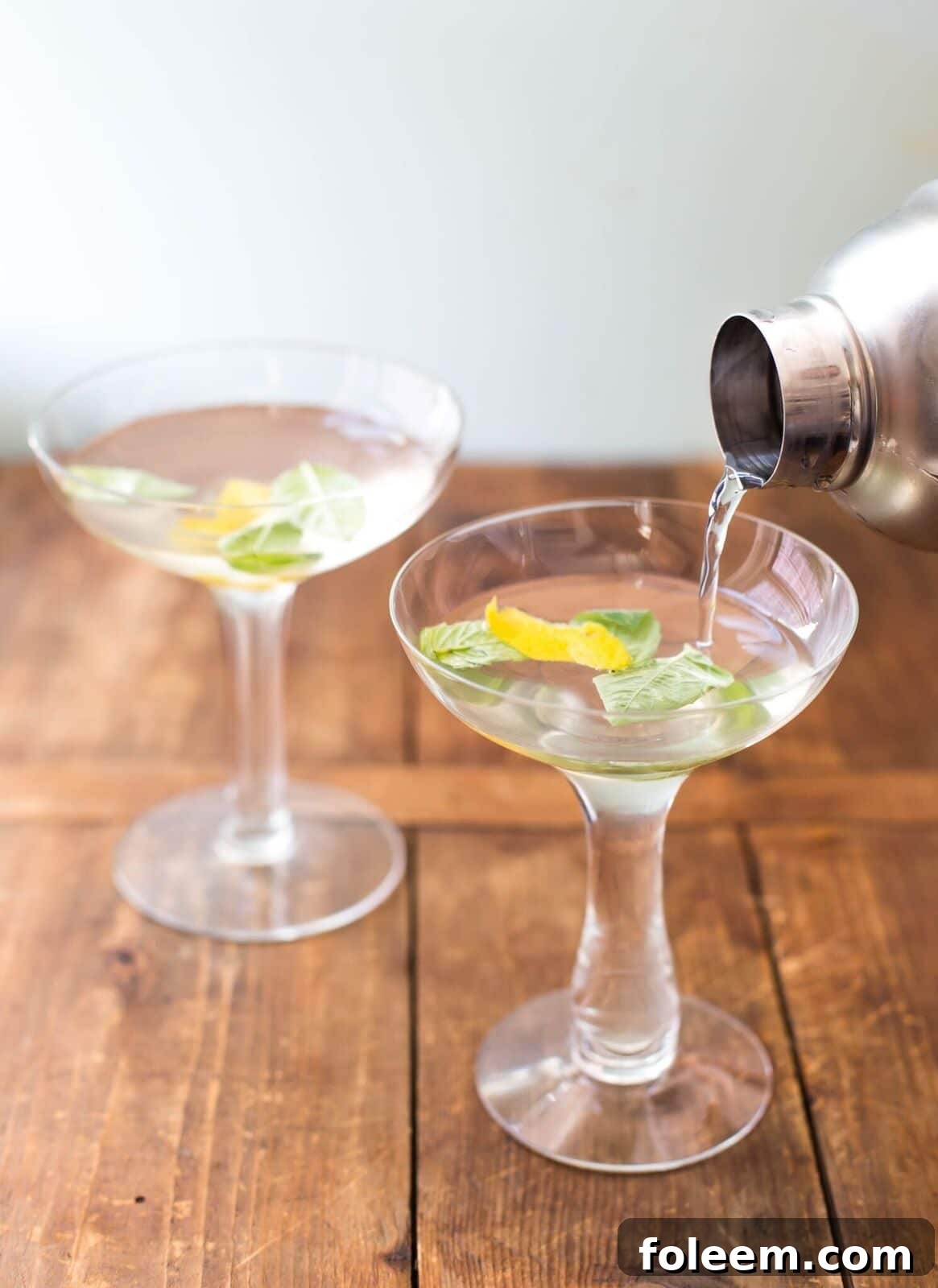 Pouring Basil Ginger Lemon Saketini from cocktail shaker into martini glasses.