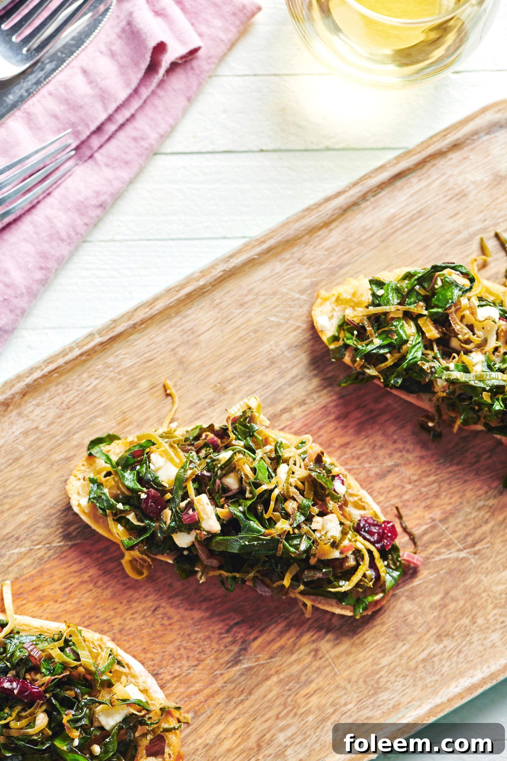 Three pieces of bruschetta topped with Swiss chard, leeks, and feta.
